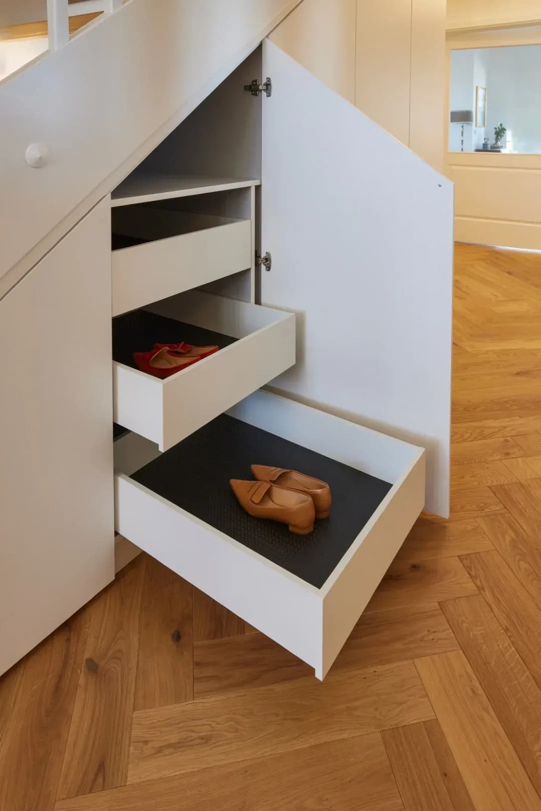 Ausgezogene weiße Schuhauszüge in einem Schrank unter der Treppe, Boden aus Eichen-Fischgrätparkett