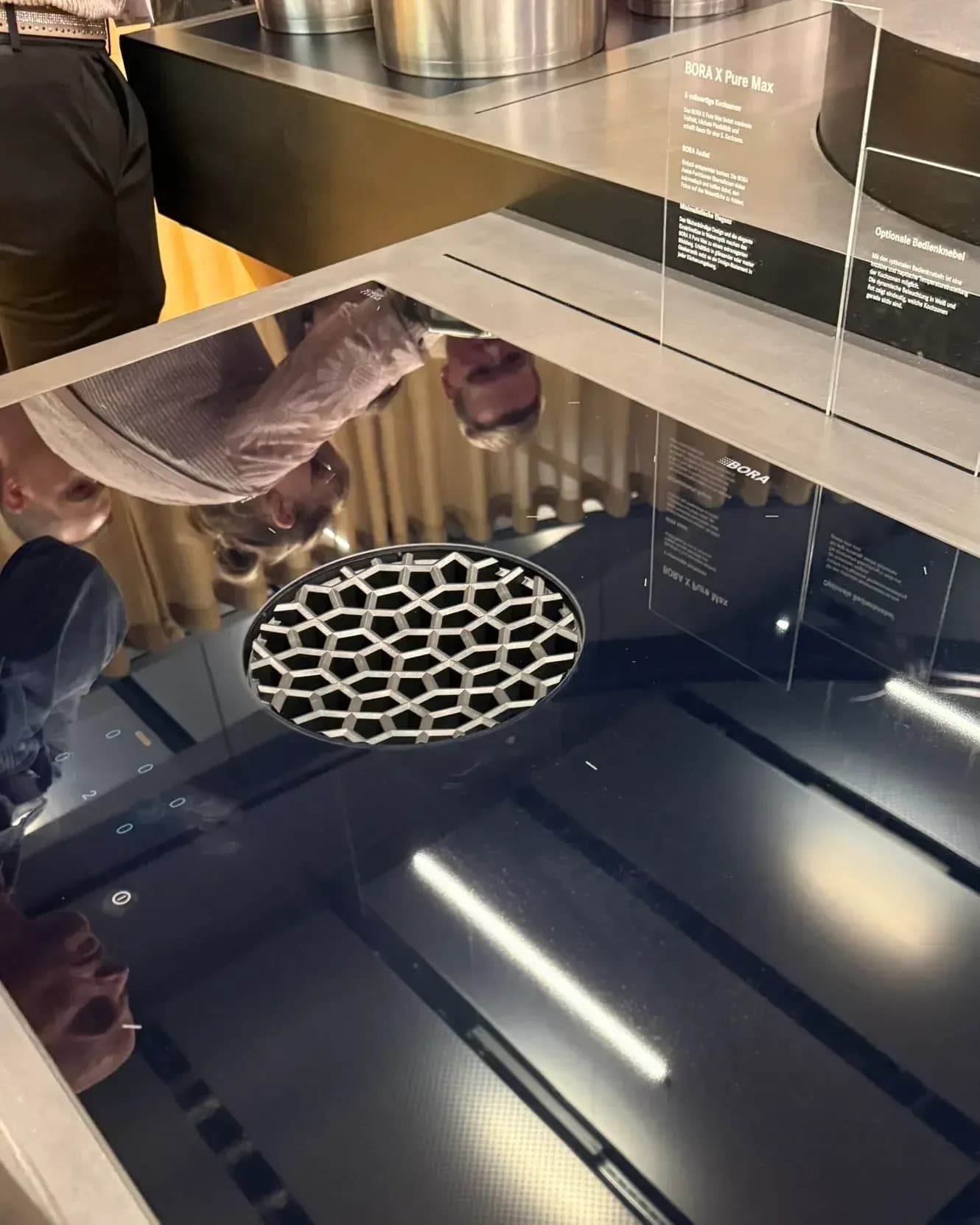 Im BORA Flagship Store in Herford auf der Küchenmeile 2026: Kochfeldabzug BORA X Pure Max mit runder Abzugsöffnung in der schwarzen Glaskeramikfläche, dahinter eine Infotafel.