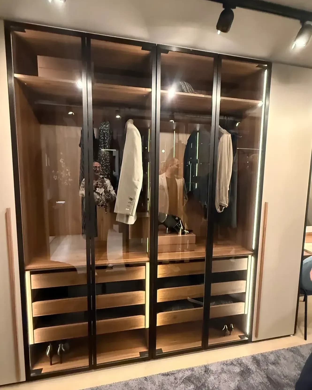 In der Architekturwerkstatt von LEICHT in Löhne auf der Küchenmeile 2026: Kleiderschrank mit schwarz gerahmten Glastüren, Innenausstattung in Holz, beleuchteten Auszügen und Kleiderstangen.