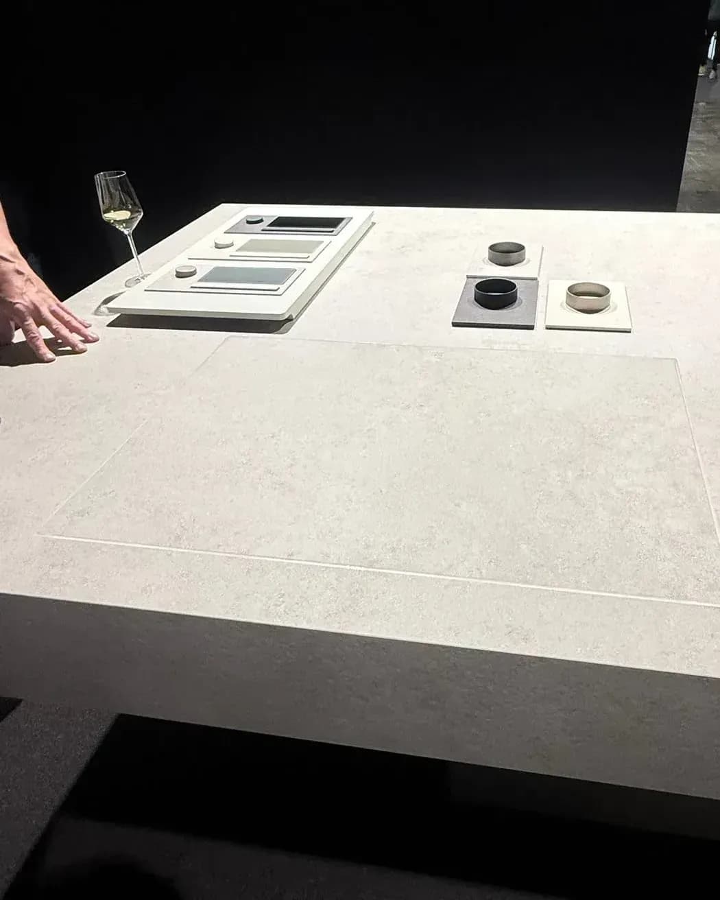 Gezeigt von V-ZUG in der Architekturwerkstatt von LEICHT in Löhne auf der Küchenmeile 2026: Tisch mit durchgehender heller Mineralfläche, in der sich das Kochfeld CookTop V6000 Integra nur als feine Kontur abzeichnet, dahinter Material- und Bedienmuster.