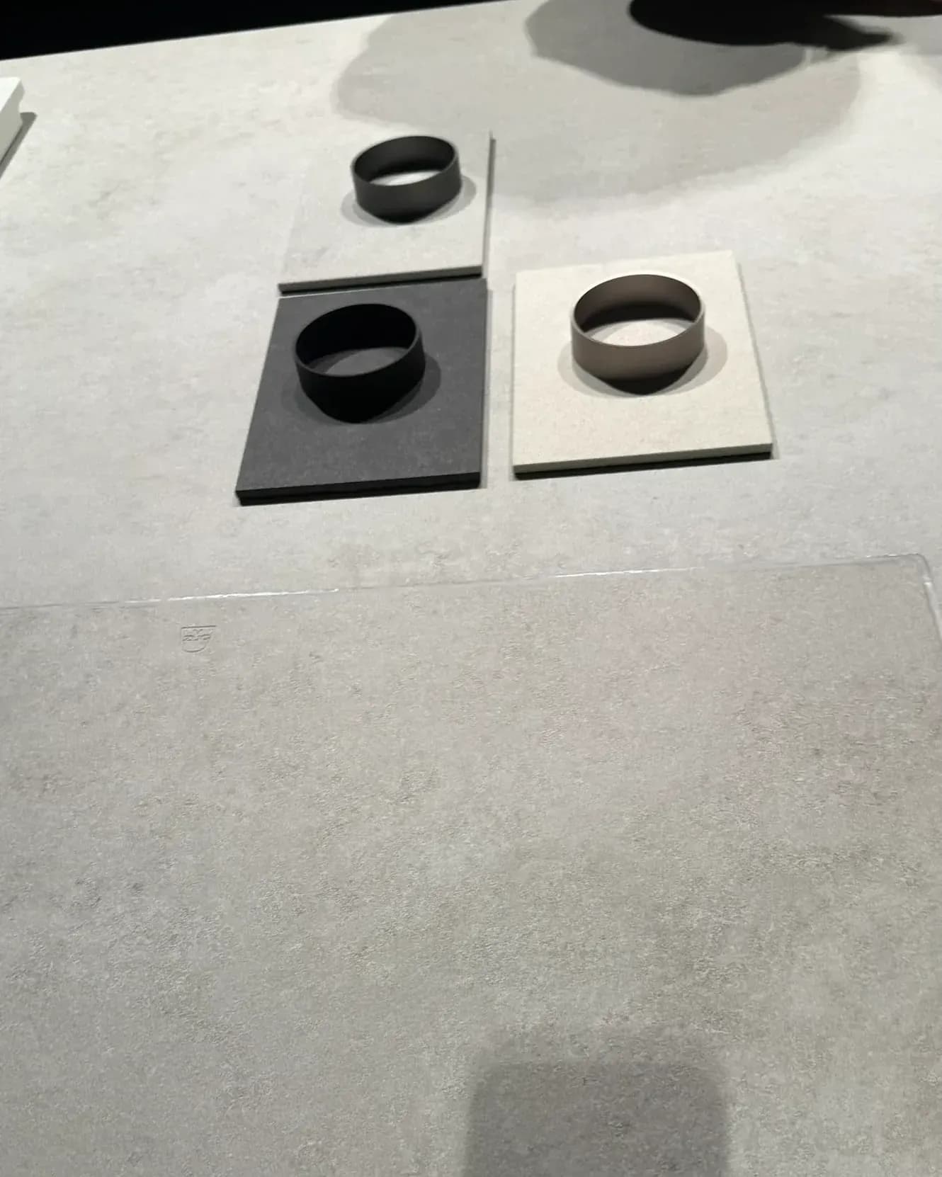 Gezeigt von V-ZUG in der Architekturwerkstatt von LEICHT in Löhne auf der Küchenmeile 2026: Nahaufnahme der hellen Mineralfläche mit der kaum sichtbaren Kontur des Kochfelds CookTop V6000 Integra, dahinter drei Materialmuster mit Ringen.