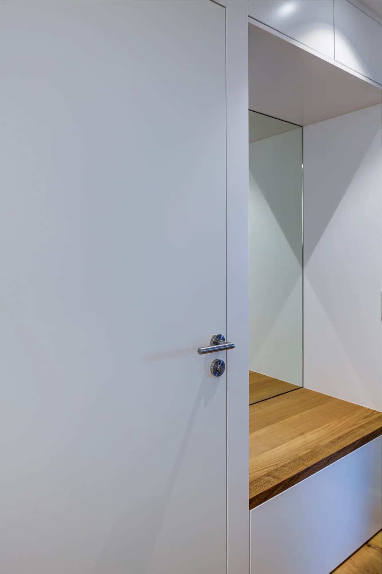 Garderobennische mit hohem Spiegel, weißem Einbauschrank und einer Sitzbank mit massiver Eichenauflage.