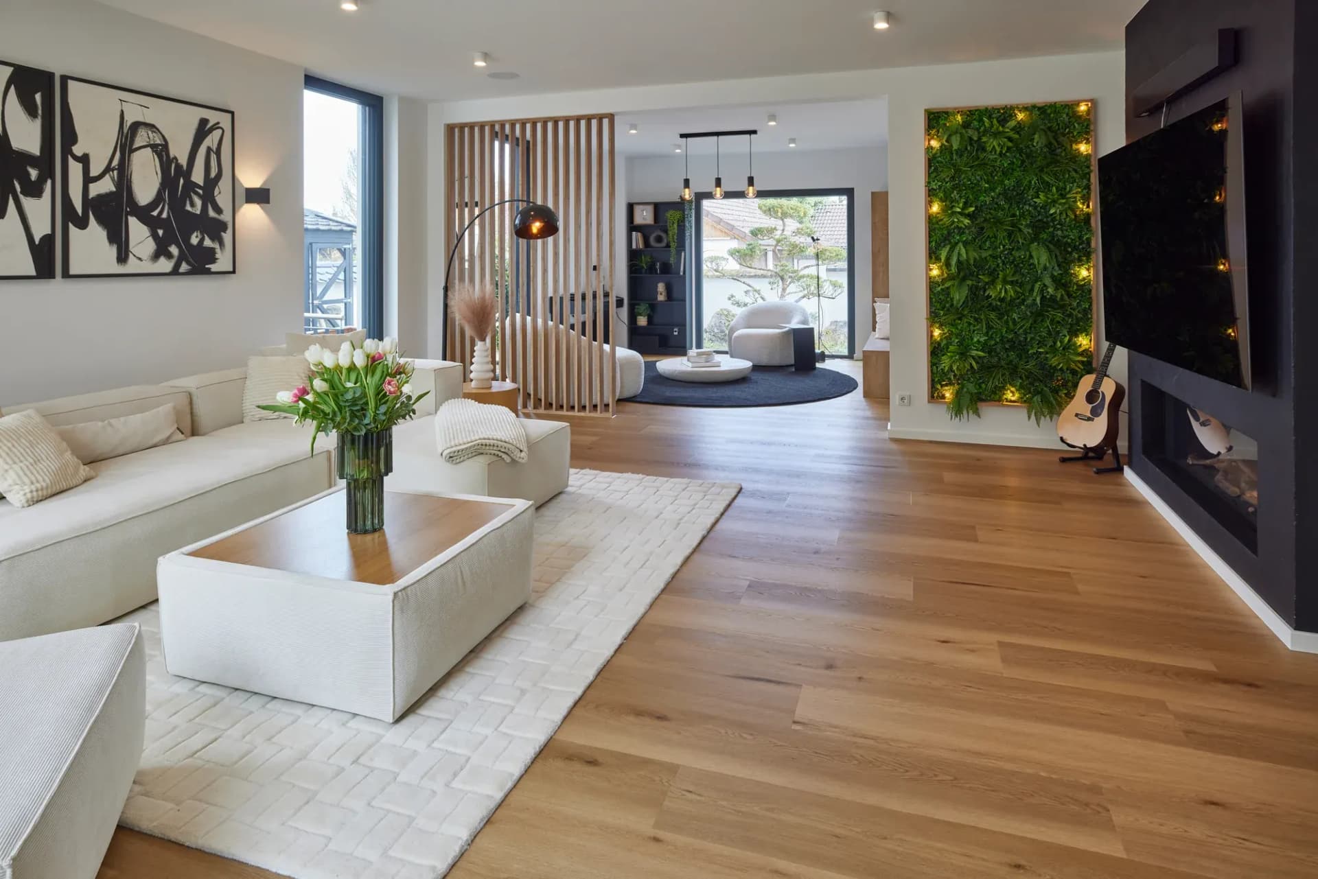 Lounge mit Kamin, begrünter Wand und hellem Sofa auf Eichenboden.