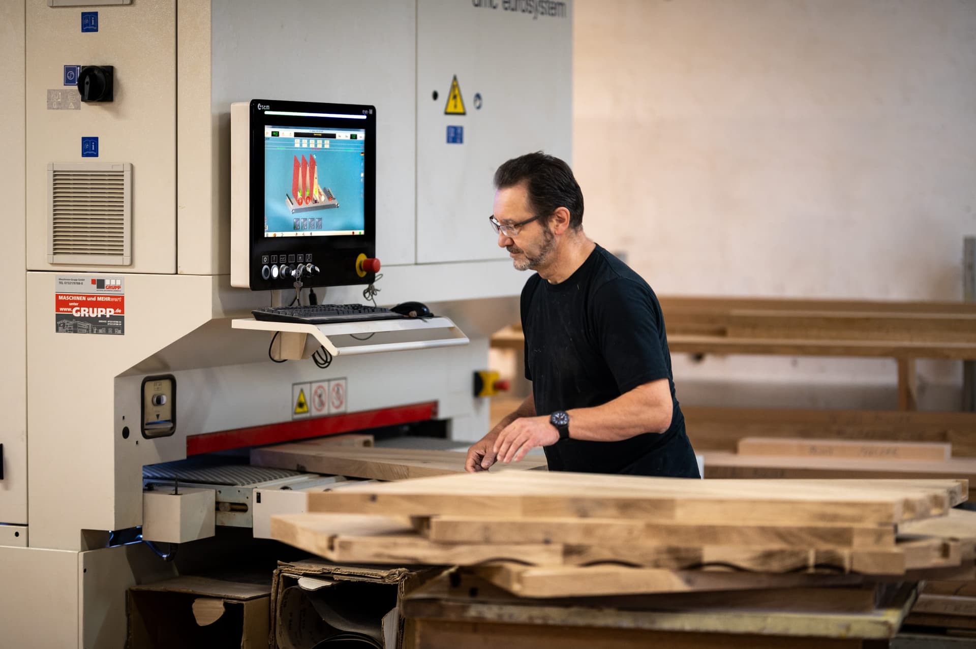 Ein Schreiner führt Massivholzbohlen in die Abrichthobelmaschine in der Werkstatt Schweighofen.