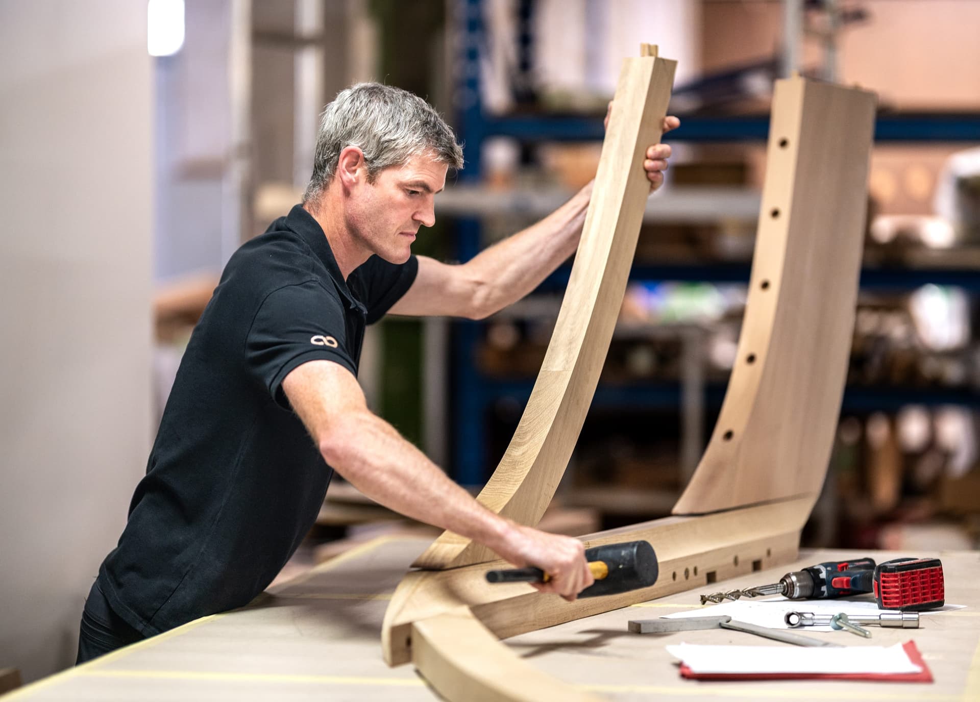 Ein Schreiner prüft ein gebogenes Massivholz-Werkstück auf der Werkbank.