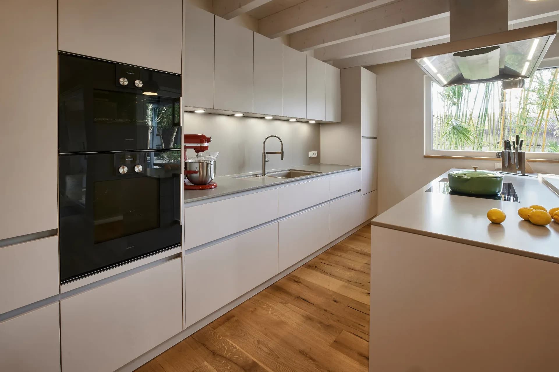 Grifflose Küchenzeile in Greige mit Gaggenau-Backöfen und Kochinsel unter einer Edelstahlhaube