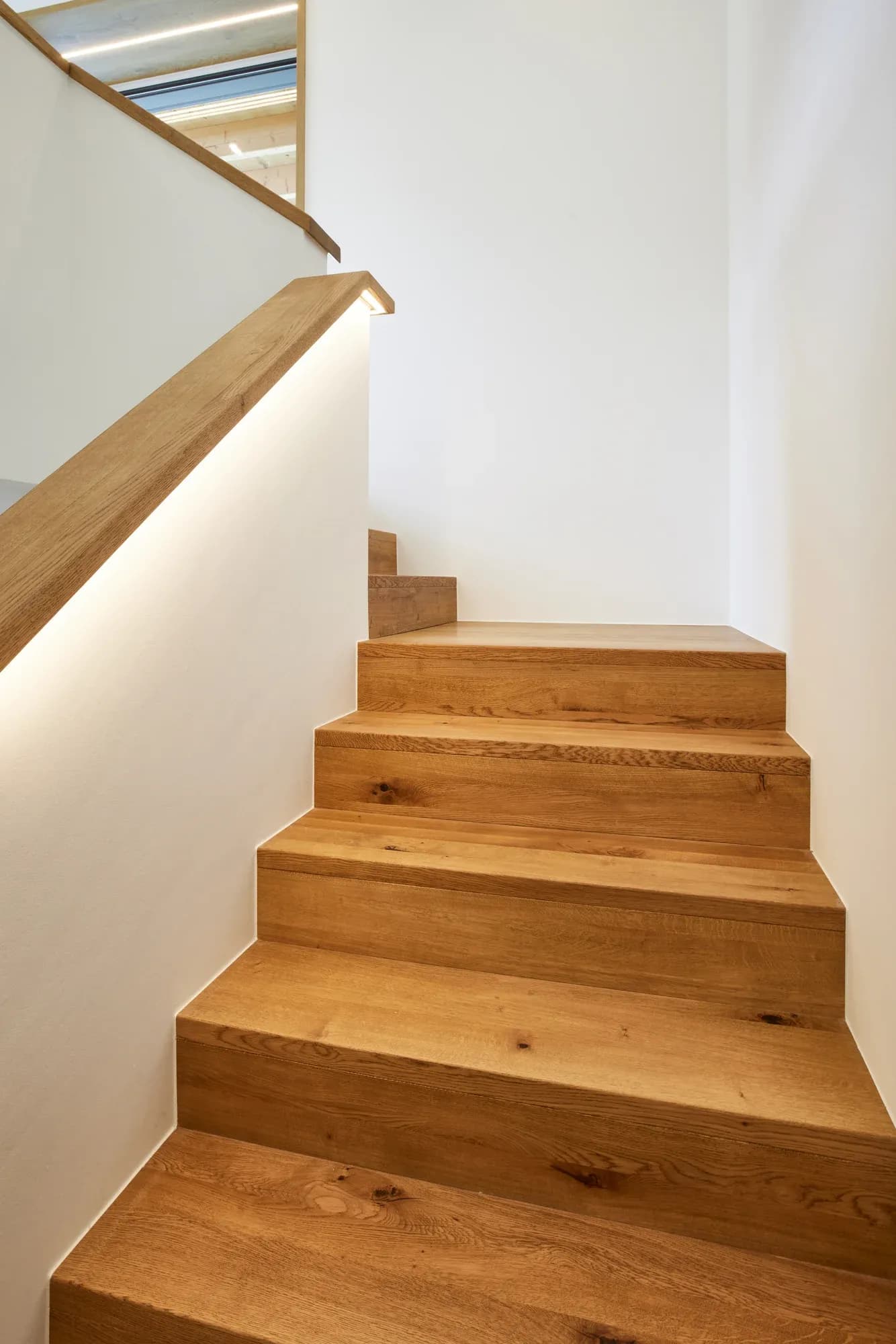 Aufblick über die Eiche-Faltwerkstufen zum Treppenauge mit indirektem Licht.