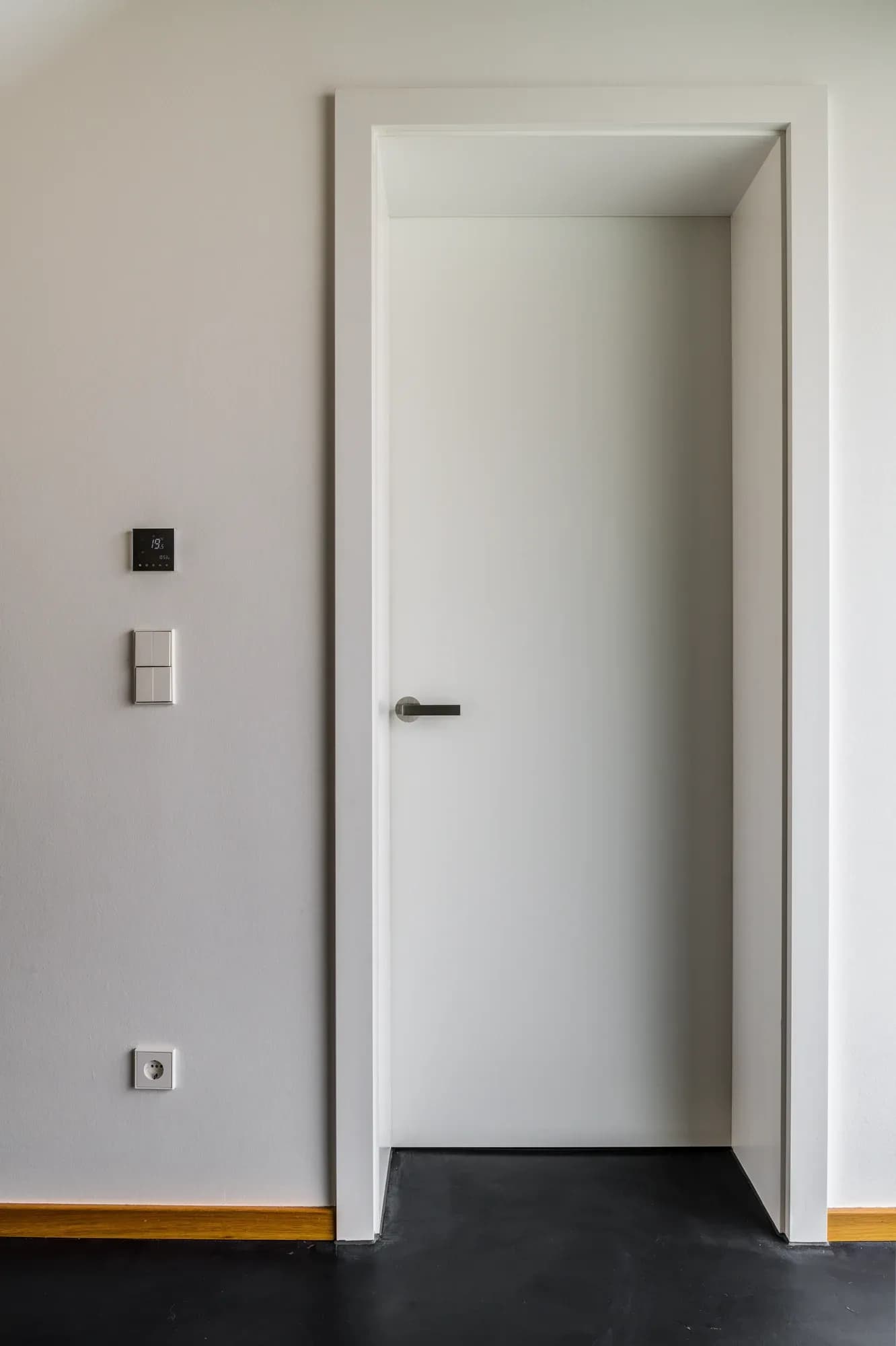 Weiße Innentür mit schmalem Griff und schmaler Zarge in heller Wand, darunter dunkler Boden und Eichen-Sockelleiste.