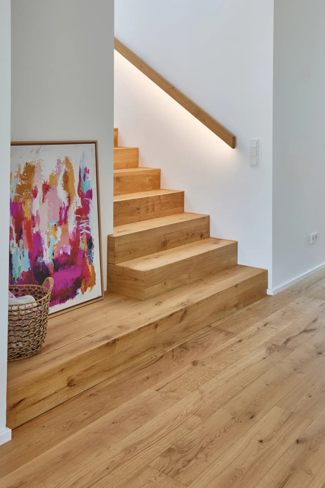 Skulpturale Faltwerktreppe aus Eiche, die gewendelt nach oben führt, begleitet von einem in die Wand eingelassenen, LED-beleuchteten Eichenhandlauf.