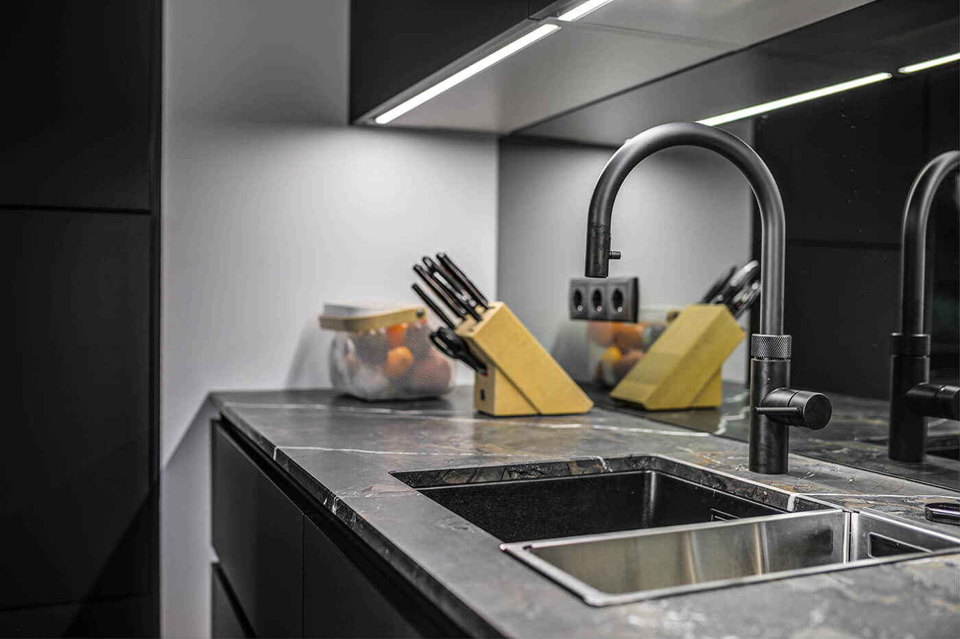 Moderne dunkle Küche mit Arbeitsplatte in Stein-Optik, Wasch- und Abtropfbecken und verspiegelter Rückwand