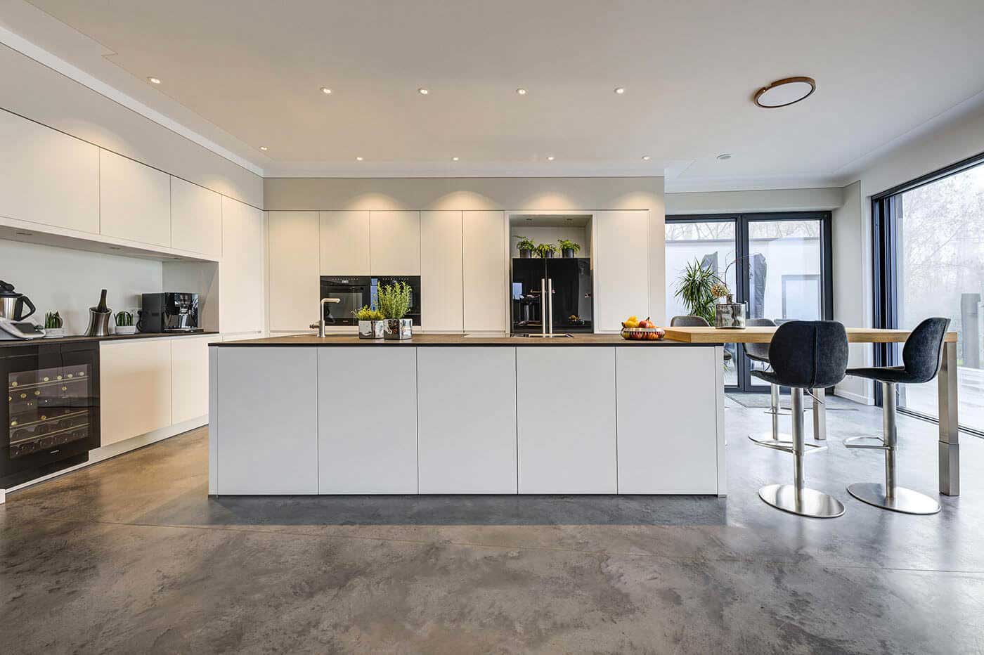 Moderne weiße Küche mit dunkler Arbeitsplatte, stylischen Elektrogeräten, Weinkühler und Holztresen
